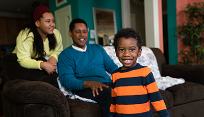 A child and their family smiles from their livingroom couch